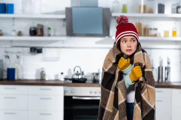 woman in full winter clothes covered in blanket due to furnace malfunction