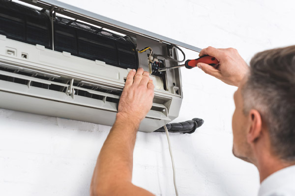 image of an air conditioner technician tightening screws on ac unit
