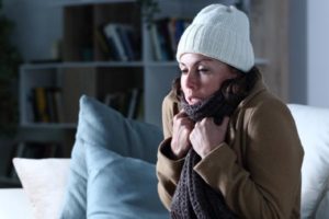 image of a cold adult woman covered with clothes freezing sitting on the sofa depicting furnace malfunction