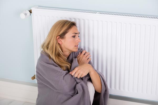 image of a homeowner sitting by radiator and boiler not producing heat