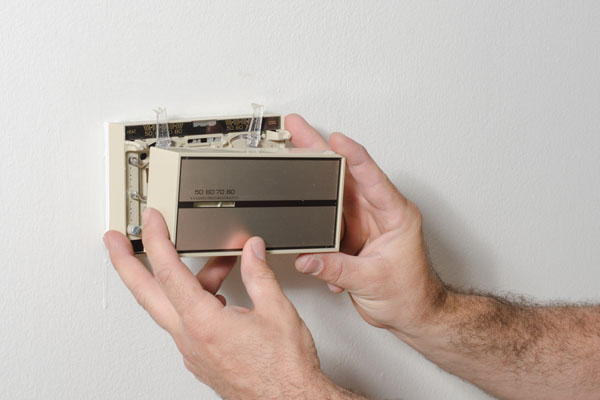 image of a homeowner removing cover of an old manual thermostat