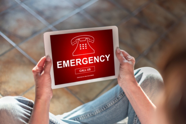 Woman sitting on the floor with a tablet showing emergency call us button depicting HVAC emergency