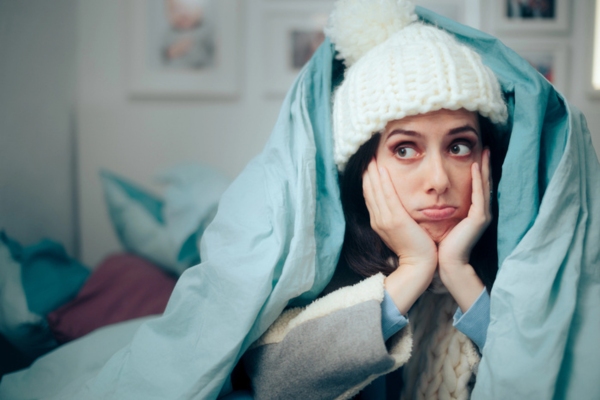 woman wearing warm winter clothes under the blanket due to no heat at home