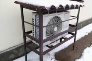 Heat pump mounted onto the wall of a house and covered in snow