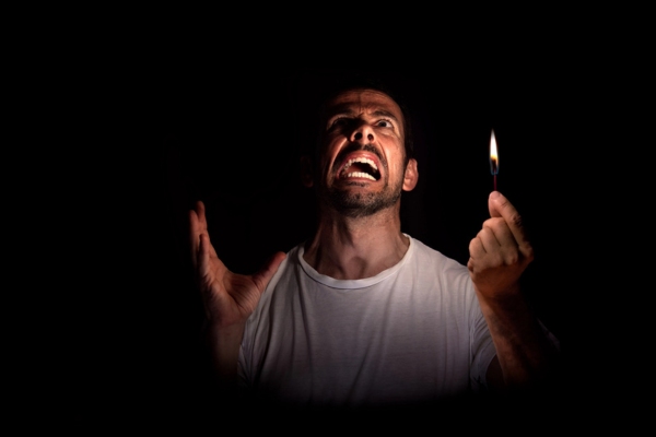 Angry man looking up while holding a match in the dark during blackout