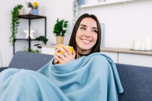 young woman holding coffee while lounging with a blanket indoors