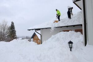 two men shoveling snow from the roof after a snowstorm
