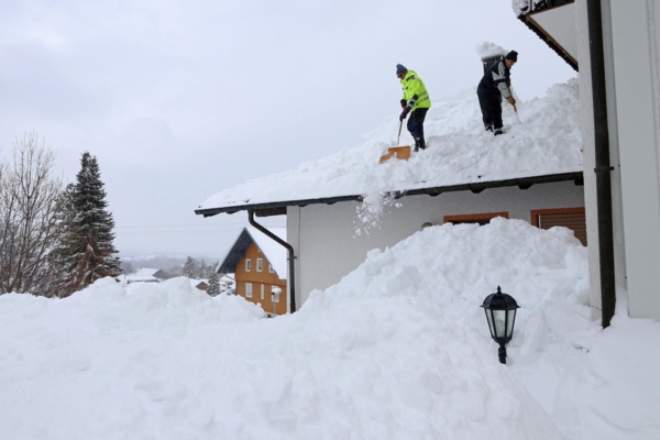 two men shoveling snow from the roof after a snowstorm