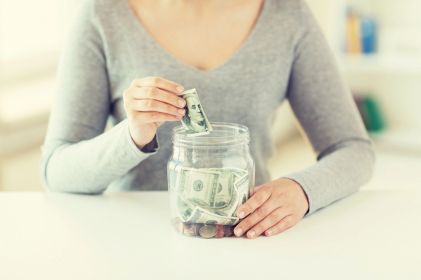 cropped image of a woman putting dollar bills in a jar depicting affordable heating oil
