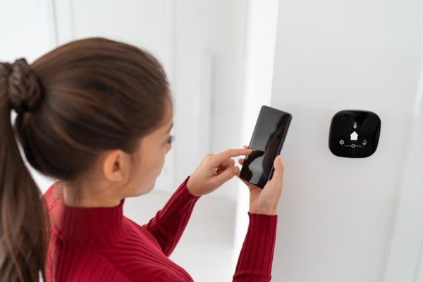 woman examining Thermostat Malfunction with smart phone in front of HVAC thermostat