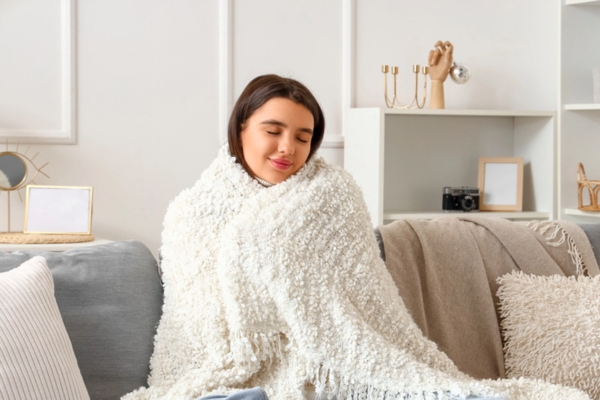 young woman hugging a blanket while sitting on the couch feeling cozy during winter