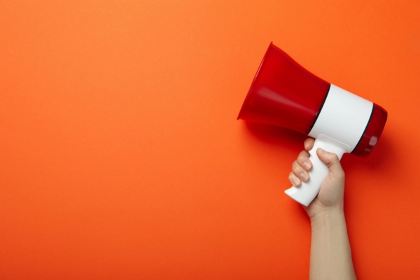 Female hand holding a megaphone on orange background depicting Warning Signs