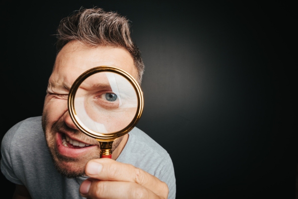 man looking through a magnifying glass depicting Identifying Warning Indicators of Leaking HVAC Air Ducts