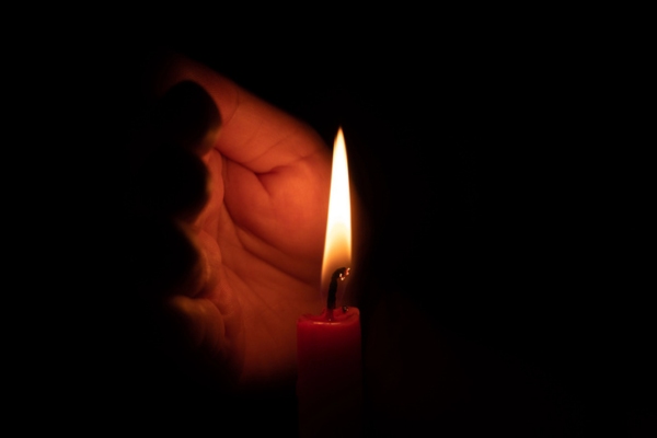 Hand protecting candle light from the wind depicting power outage