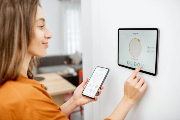 woman adjusting and synching thermostat on her smart devices